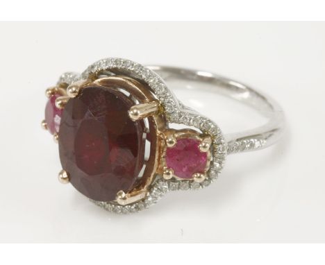 A ruby and diamond ring, with a central oval mixed cut ruby, glass filled, a small ruby to each side, with an outer border of