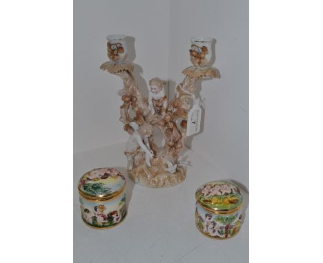 A continental double candlestick moulded with two cherubs playing among foliage ; a Capo Di Monte  circular pot and cover ; a