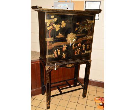 A 20TH CENTURY ORIENTAL BRASS BANDED TWO DOOR CABINET, on a seperate square frame base, black ground with painted Japanese fi