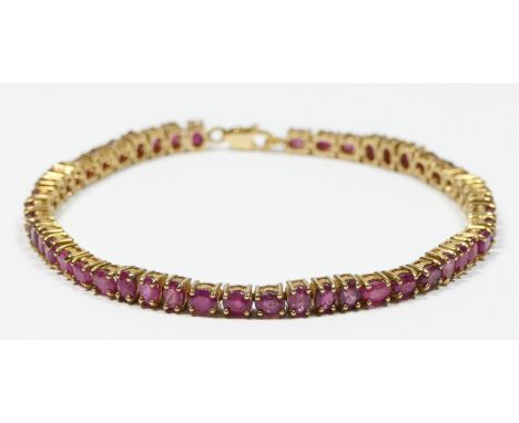 A 10 k gold and ruby set line bracelet, claw set with three oval mixed cuts stones mounted vertically followed by three horiz