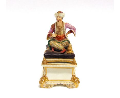 A BLOOR DERBY FIGURE OF AN ARAB  seated on a cushion smoking a hookah pipe, on square pedestal base with mask corners, 15cm h