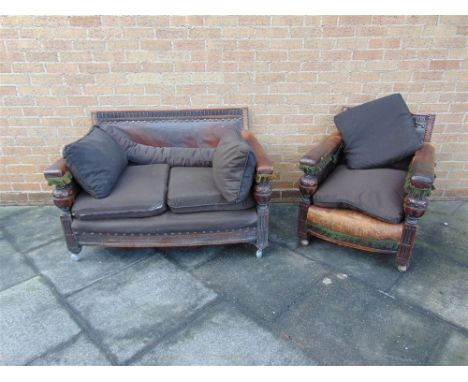 A CARVED OAK FRAMED TWO SEATER SOFA  and matching armchair, with distressed leather upholstery, the sofa 126cm wide 85cm deep