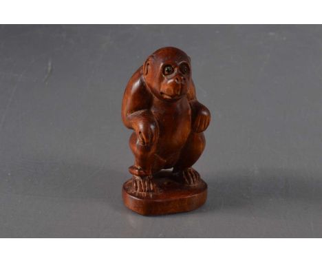 A Japanese boxwood netsuke in the form of a seated monkey, the face with inlaid eyes. Signed to the base. 6.8 cm high.