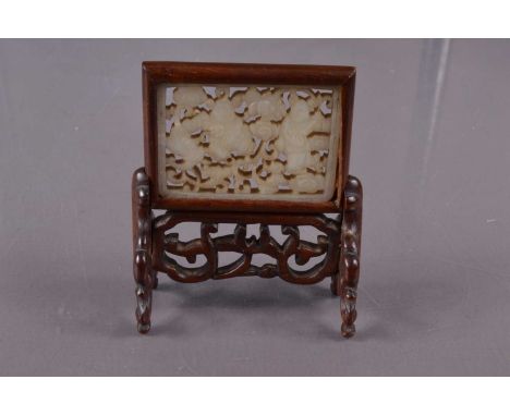 A Chinese reticulated jade plaque mounted as a miniature table screen, the mutton fat jade plaque carved with two dancing fig