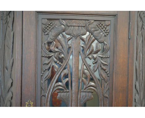 An Arts and Crafts or Art Nouveau style carved oak corner cabinet, the dark oak frame in two sections. The top with a glazed 