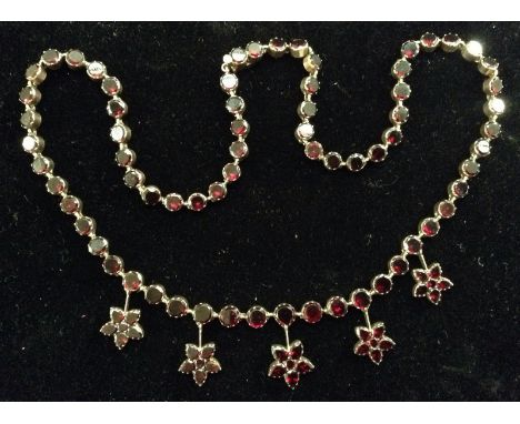 An Edwardian red garnet fringe necklace, the main panel suspended with five six stone flower head drops, each articulated rou