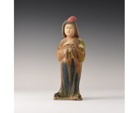 An undated archaistic polychrome glazed ceramic figurine of a courtly lady standing with hands in the folds of her sleeved; h