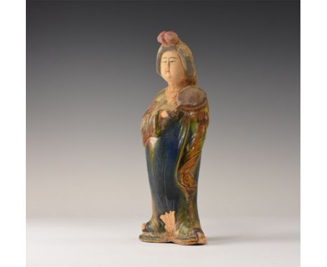 An undated archaistic glazed ceramic figurine of a courtly lady standing with hands in the folds of her sleeved; hollow to th