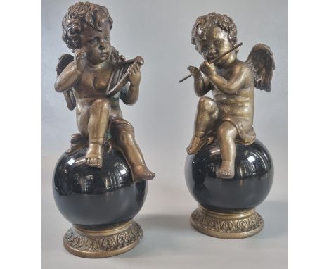 Pair of bronze seated musical cherubs playing the flute and harp, on glass globular and gilded bases.  26cm high approx.  (2)