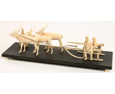 AN INUIT MARINE IVORY MODEL OF A FAMILY OF THREE, SLED AND THREE REINDEER, EARLY 20TH C, ON BLACK PAINTED WOOD BASE, 36CM L, 