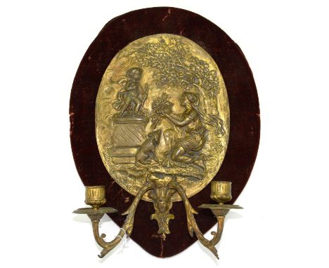A GILT BRASS TWIN BRANCH WALL LIGHT, THE BACK PLATE IN THE FORM OF AN OVAL PLAQUETTE OF A WOMAN KNEELING AT THE ALTAR OF LOVE