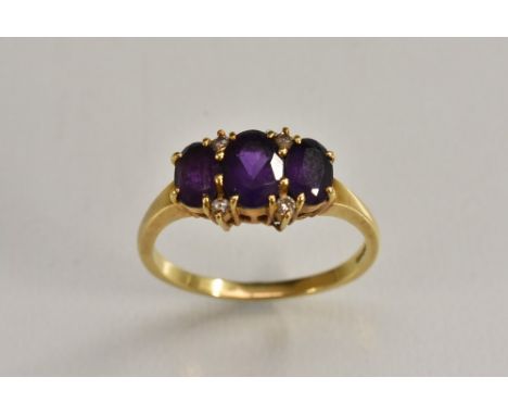 An amethyst and diamond line ring, trilogy of oval deep purple amethysts each divided by a pair of diamond accents, 18ct gold