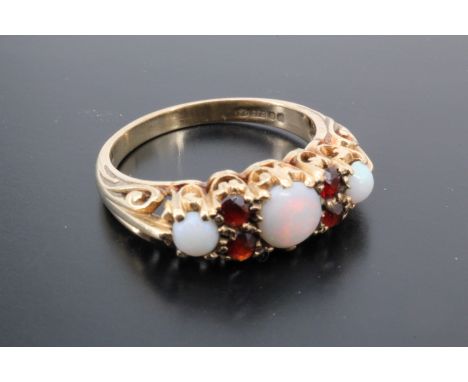 A 1970s opal and garnet ring, comprising three round opal cabochons, the central stone 5 mm, divided by pairs of small facet-