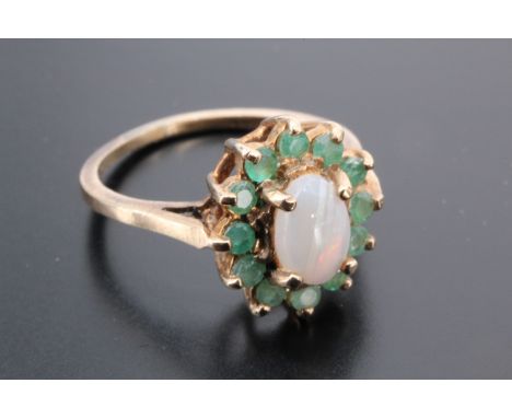 An opal and emerald ring, comprising an oval opal cabochon (7 mm x 4 mm), claw-set within a frame of emeralds on a 9 ct gold 