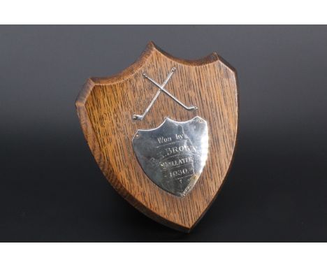 An early 20th Century golfing trophy, formed as an oak shield with a pair of crossed silver golf clubs over a silver shield w