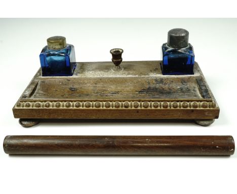 An Edwardian oak ink standish, carrying a pair of facet-cut blue glass ink wells, one having a silver cap,  34 cm x 18 cm, to
