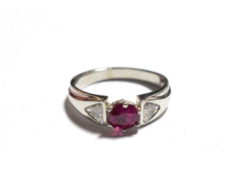 A ruby type and diamond ring, an oval cut ruby type in a white claw setting, flanked by trilliant cut diamond channel set sho