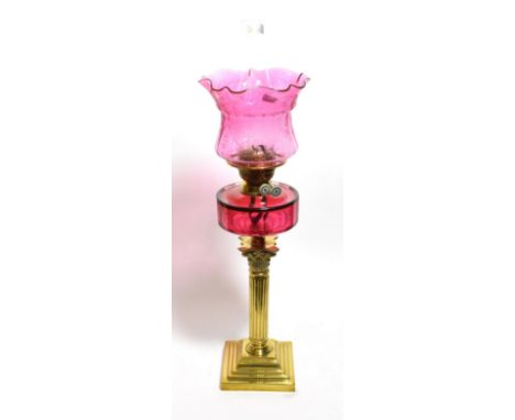 A Victorian oil lamp with a brass Corinthian column base and cranberry tinted shade 