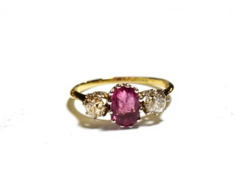 A ruby and diamond ring, an oval mixed cut ruby flanked by two old cut diamonds in white claw settings, to a yellow tapered s