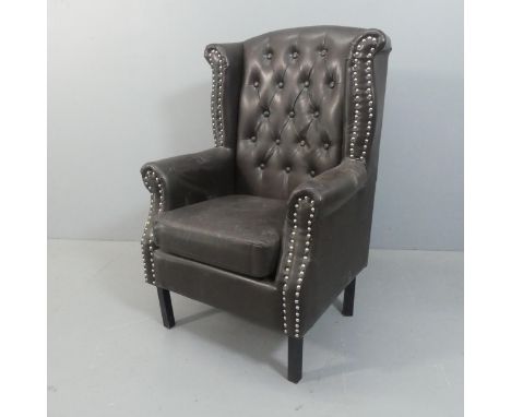 A studded button-back faux-leather upholstered winged armchair.