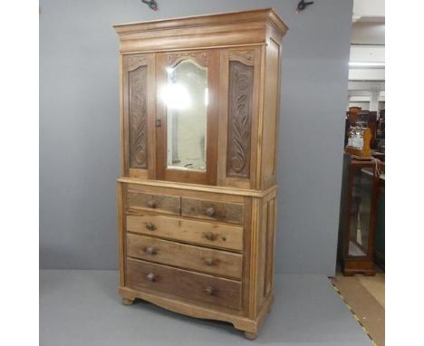 An Art Nouveau style two-section pine cabinet on chest, with single mirrored door, carved decoration and two short and three 