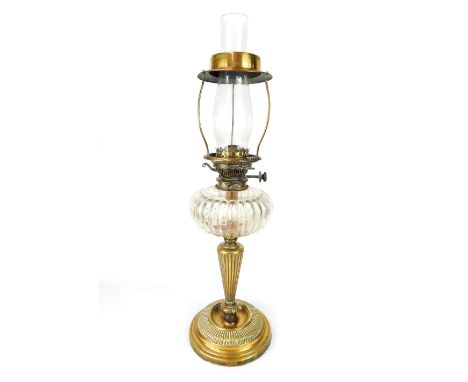 A victorian oil table lamp with clear glass chimney over lobed glass reservoir raised on reeded brass stem on circular brass 