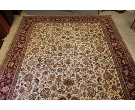 A PERSIAN CARPET, the ivory field with all over bold design of scrolling foliage and flowers in colours within a similar clar