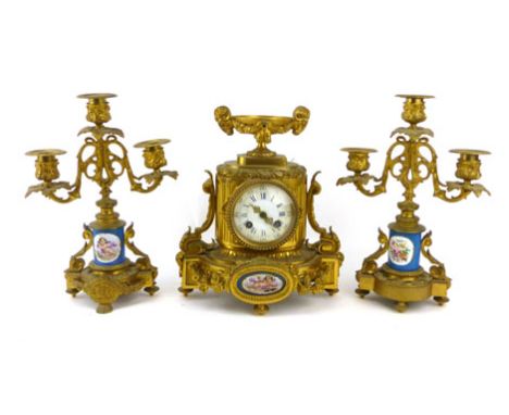 A late 19th century French gilt metal clock garniture with a rams head urn over a circular enamelled dial in a fluted oval ca