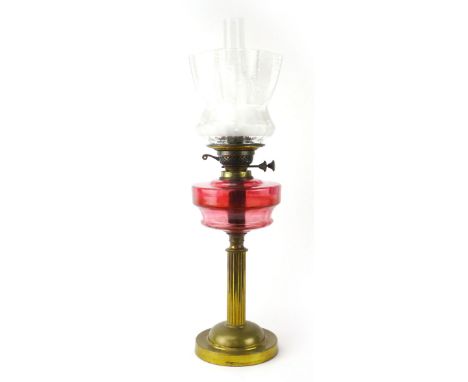 A Victorian oil burning lamp with cranberry glass paraffin burner, etched glass shade, clear glass chimney, brass single pede