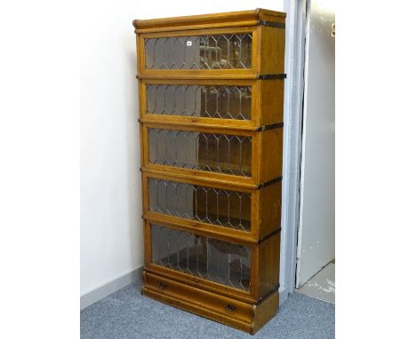 A GLOBE WERNICKE LIGHT OAK FIVE SECTION BOOKCASE with lower drawer base and shaped cap, the doors with leaded glass, 177 cms 
