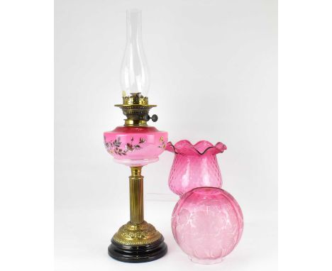 A Victorian oil lamp with faded opaque and red glass font with over floral enamel, raised on brass Corinthian column and dome