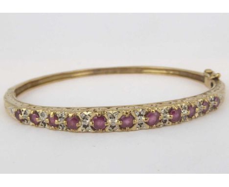 A late 19th/early 20th century yellow metal ruby and diamond hinged bangle with eleven graduated rubies separated by double r