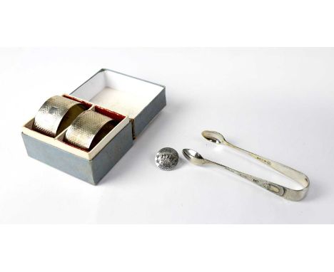 A pair of boxed hallmarked silver engine turned napkin rings, a pair of plated silver sugar tongs, and a silver button pin wi