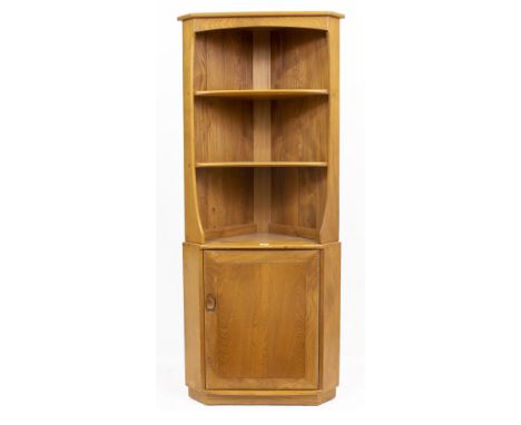 AN ERCOL LIGHT ELM CORNER CABINET with two fixed shelves above a cupboard door below, raised on a plinth base, 74cm wide x 49