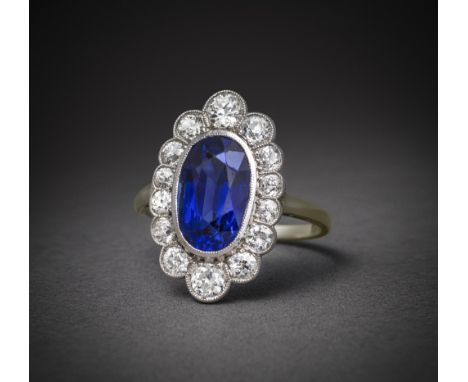 A sapphire and diamond ring, early 20th century, of cluster design, millegrain-set with an oval sapphire weighing 4.69 carats