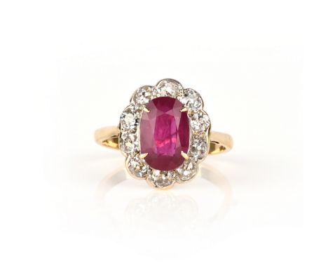 A ruby and diamond cluster ring, the oval-shaped ruby is set within a surround of old circular-cut diamonds in platinum and g