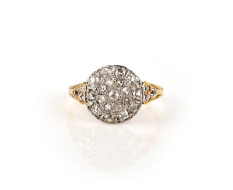 A diamond ring, the disc-shaped centre pavé-set with cushion-shaped diamonds, to shoulders each set with a trio of additional