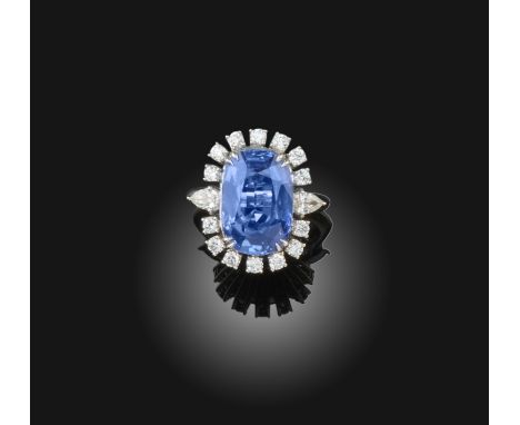 A sapphire and diamond cluster ring, the cushion-shaped sapphire is set within a surround of round brilliant-cut diamonds, wi