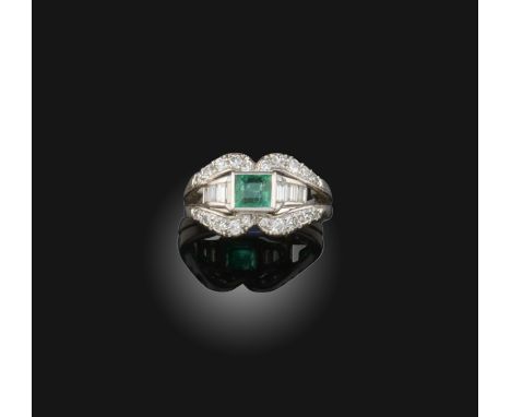 A mid 20th century emerald and diamond ring, set with an emerald within scrolling shoulders set with baguette-shaped and circ