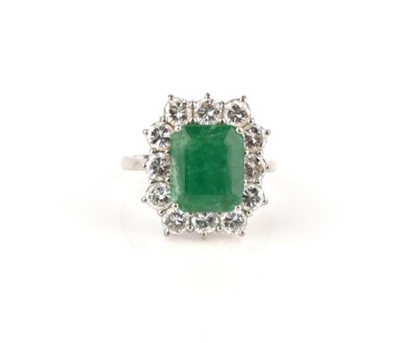 An emerald and diamond cluster ring, the emerald-cut emerald weighs approximately 2.90cts, set within a surround of round bri