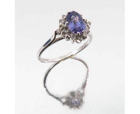 An 18 carat white gold Tanzanite and diamond cluster ring, the oval cut enclosed by fourteen small brilliant cuts and one dia