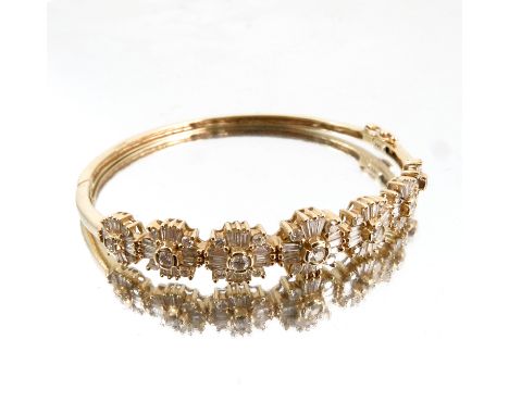 A diamond hinged bangle, stamped '14k', the frontispiece of seven clusters with a central brilliant cut, twelve tapering bagu