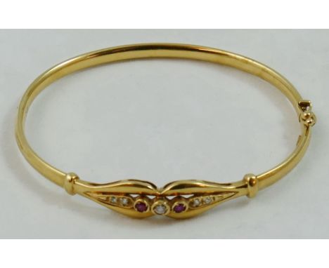 A 9ct gold hinged bangle, the openwork scroll front set with graduated red and colourless stones, weight 7 grams.