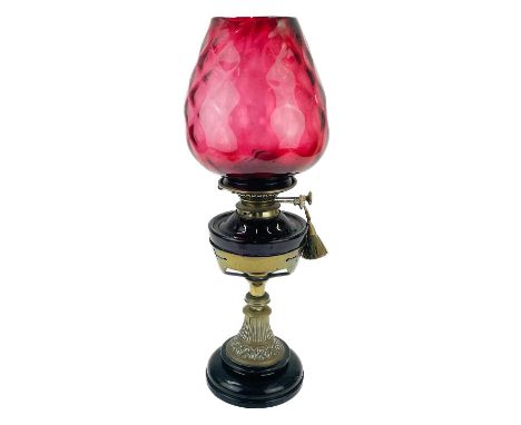 A Victorian brass oil lamp with a cranberry glass shade.  Raised on a circular base, with a glass oil reservoir, height 54cm.
