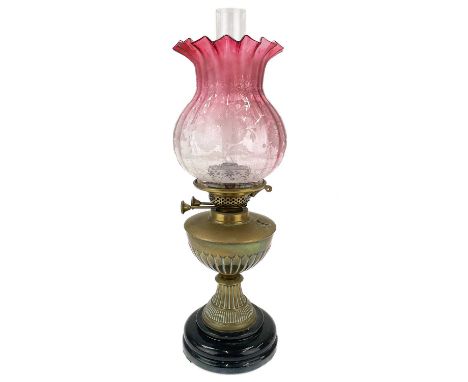 A Victorian brass oil lamp with cranberry etched glass shade.  Raised on a circular base, with brass oil reservoir and a cran