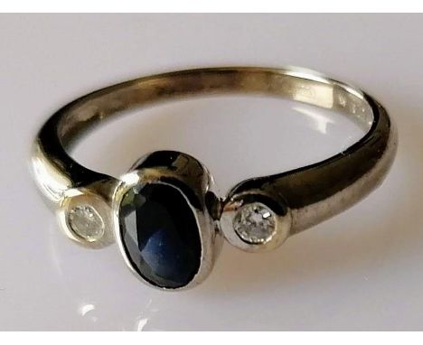 A 9ct white gold three-stone sapphire and diamond rub over ring; the oval sapphire 6mm x 4mm estimated 0.55 carat, size M 1/2