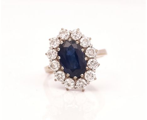 A 18CT WHITE GOLD, SAPPHIRE AND DIAMOND SET OVAL CLUSTER RINGClaw set with the oval cut sapphire in a surround of twelve circ