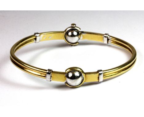 A yellow and white metal (tested high carat gold, with an Arabic hallmark) bangle, L. 17.5cm, (approx. 23.4gr).