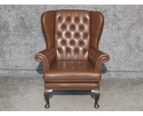 Brown leather metal studded wing back armchair, button back with mahogany feet