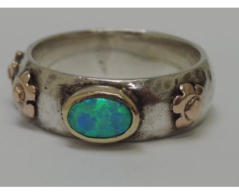 A white metal band having a black opal in a collared mount with yellow metal floral applique decoration, no marks previously 